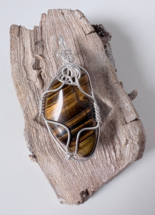 Silver pendant with a tiger's eye stone on a piece of driftwood against a white background