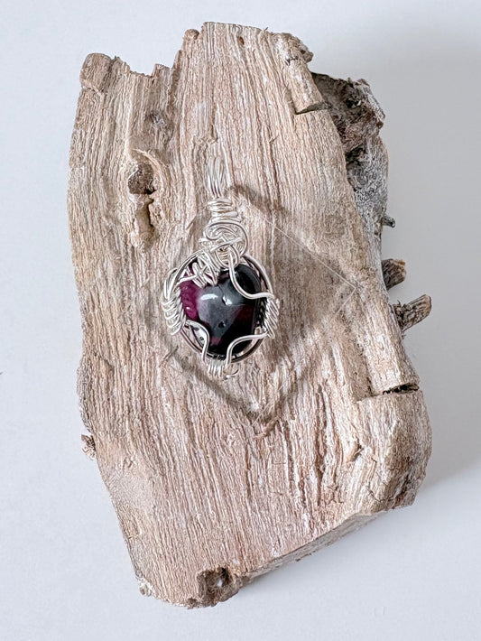 Silver wire-wrapped garnet pendant on a piece of driftwood against a light background