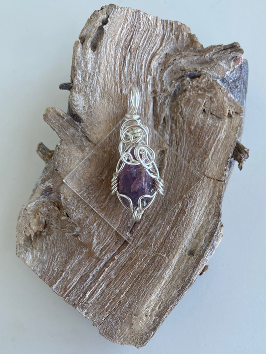Lepidolite Pendant – Back view of a wire-wrapped purple lepidolite stone pendant, handcrafted in silver-plated copper wire with a unique spiral design — photographed on a wood surface.