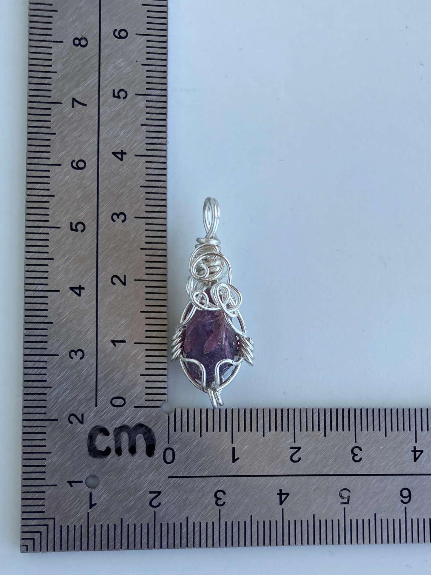 Lepidolite Pendant – Back view of a wire-wrapped purple lepidolite stone pendant shown beside an L-shaped centimeter ruler for size reference. Handcrafted in silver-plated copper wire with a unique spiral design — photographed on a white surface.