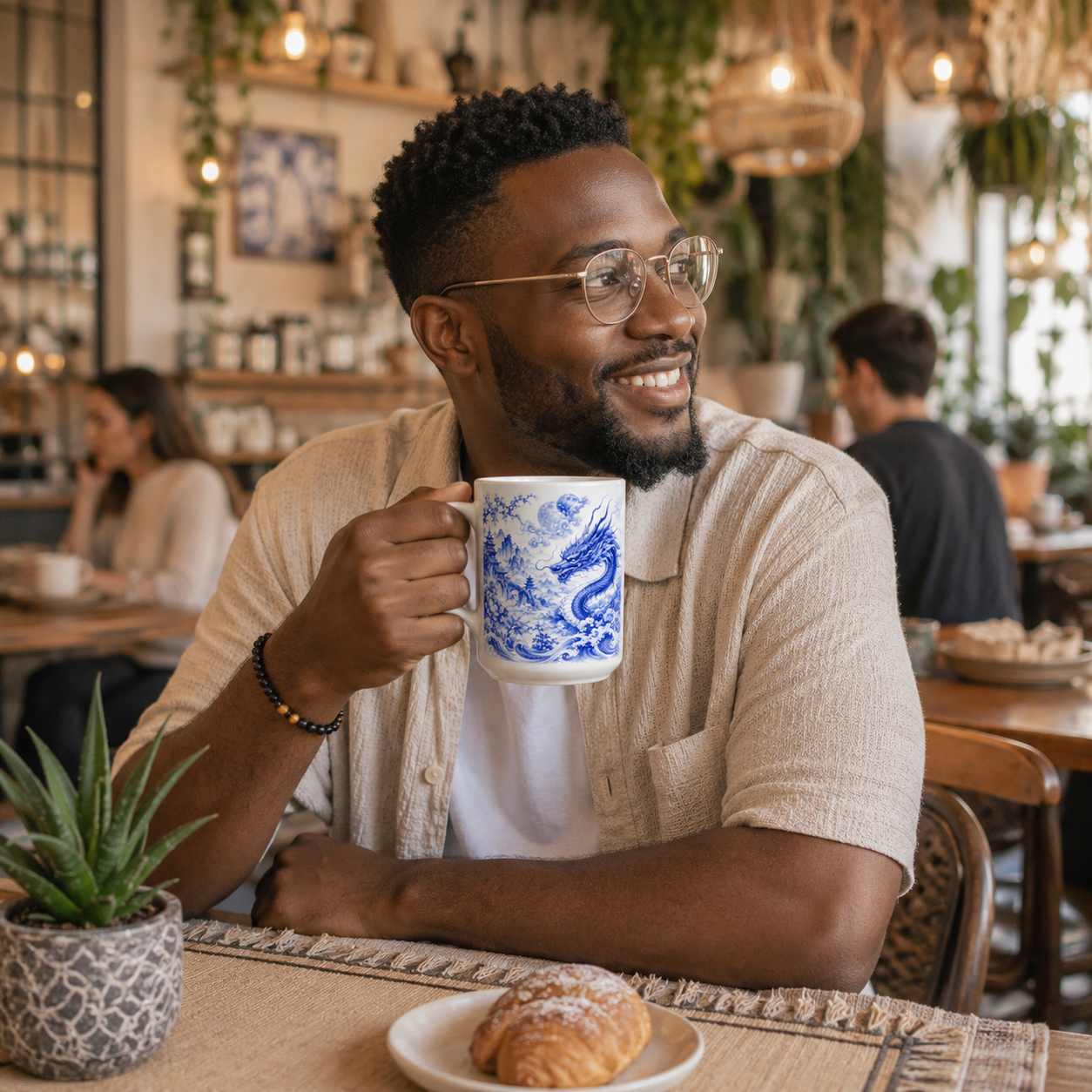 Man sitting at a cafe holding a white mug with a blue dragon design, smiling.