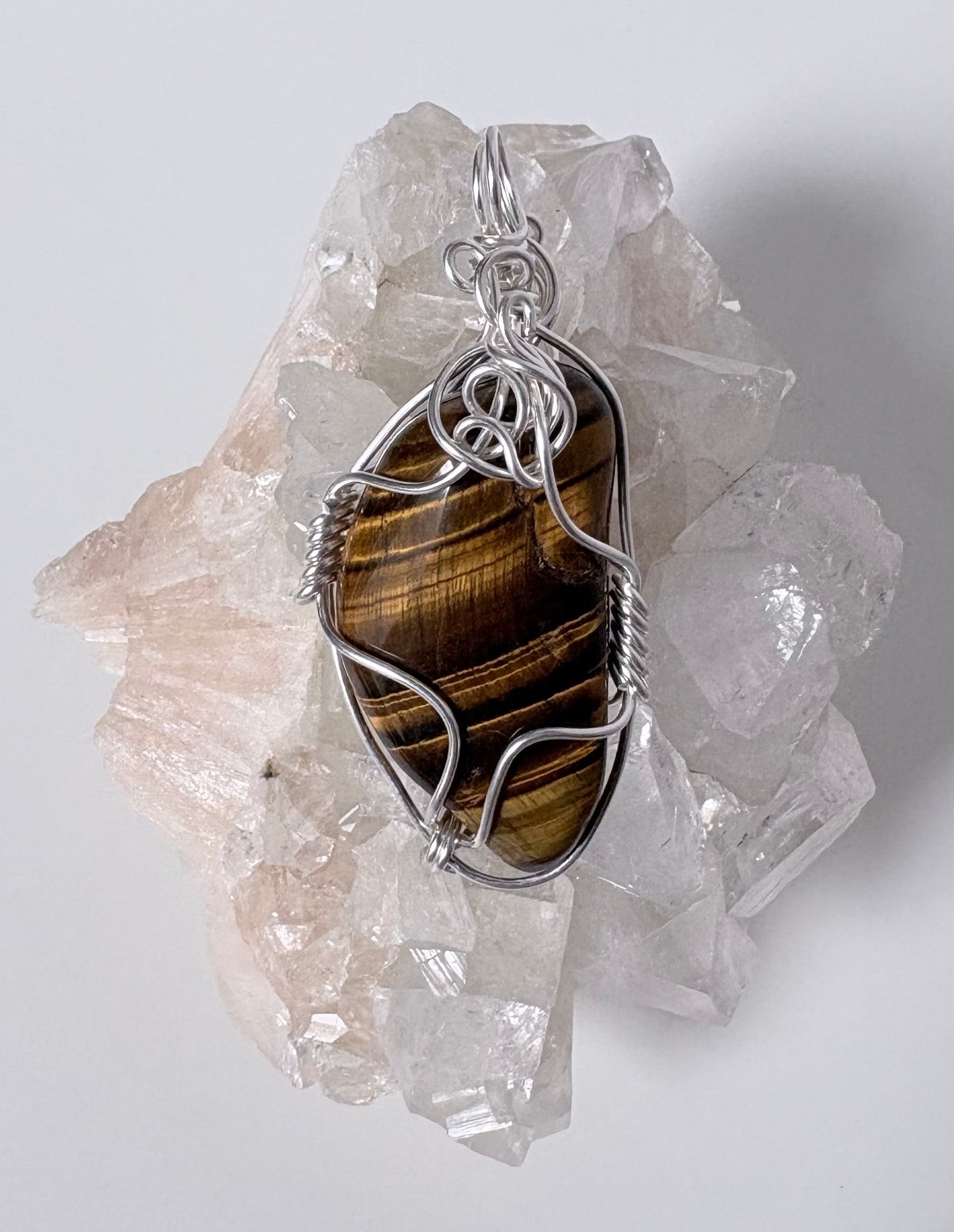 silver wire wrapped tigers eye pendant on a  clear crystal cluster with a light gray background