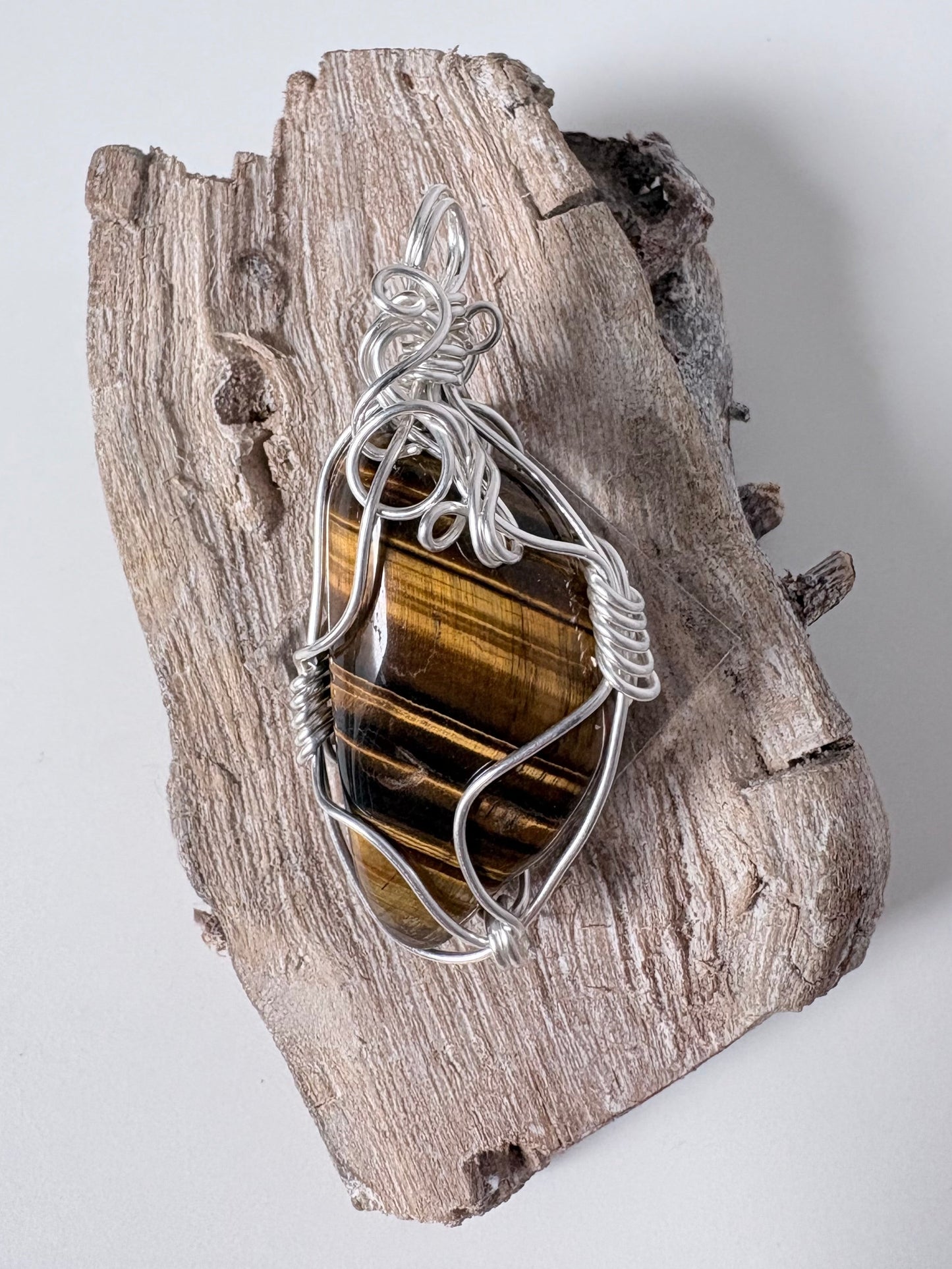 Silver pendant with a tigers eye stone on a piece of driftwood against a white background