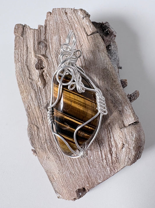 Silver pendant with a tigers eye stone on a piece of driftwood against a white background