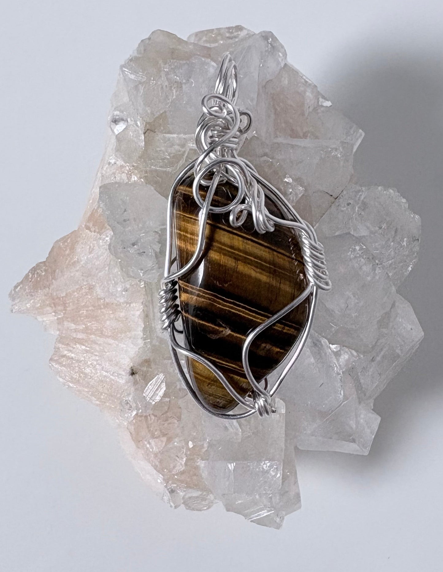 silver wire wrapped tigers eye pendant on a  clear crystal cluster with a light gray background