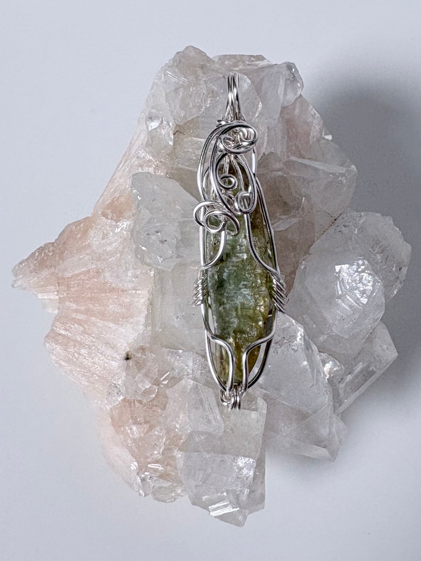 silver wire wrapped green kyanite pendant on clear crystal cluster with a white background