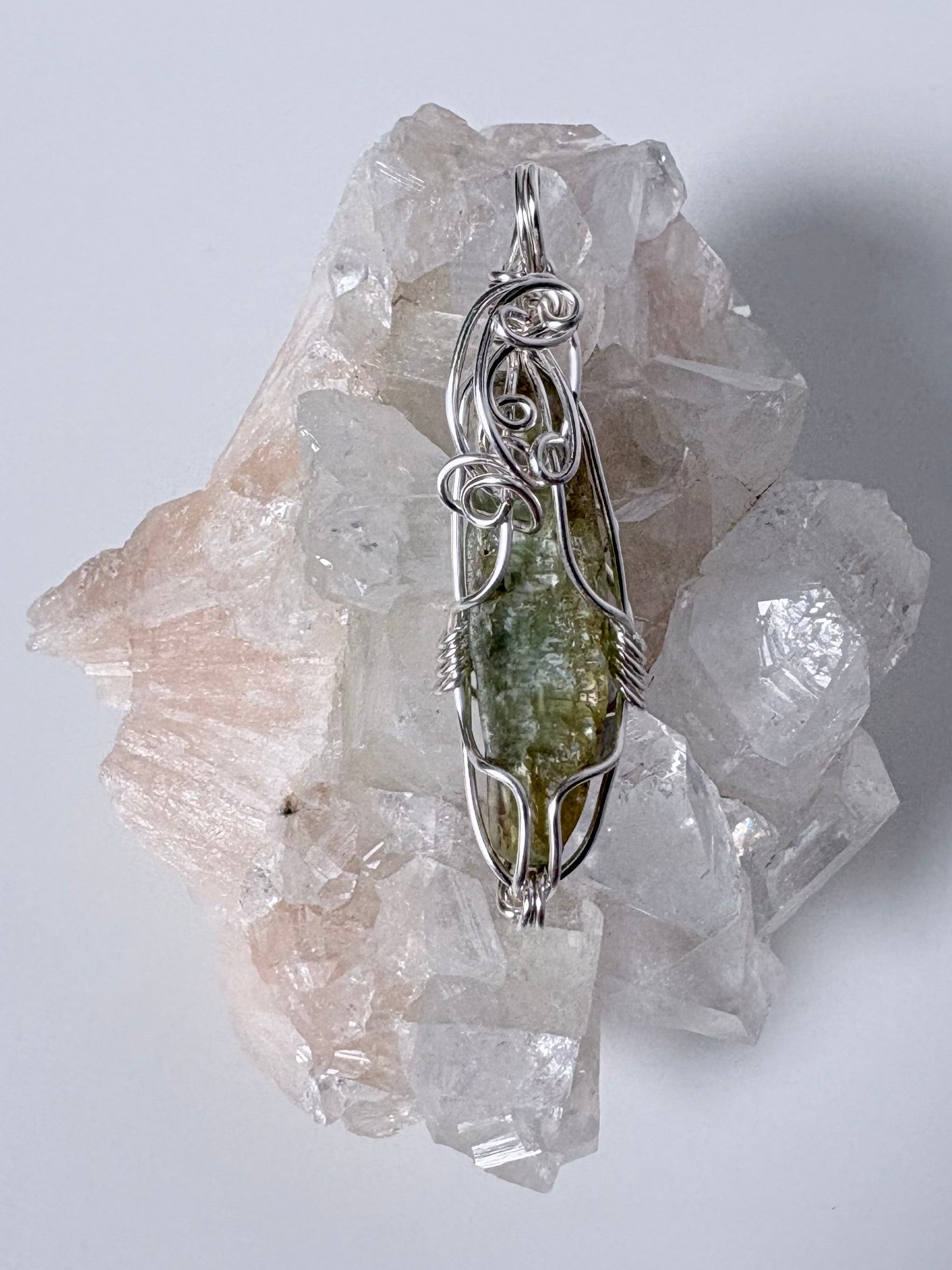 silver wire wrapped green kyanite pendant on clear crystal cluster with a white background