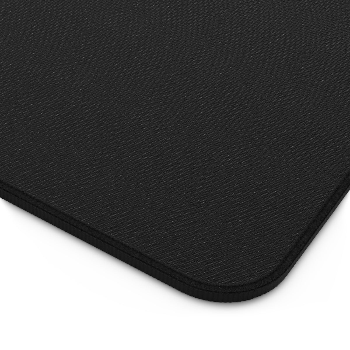 Close-up of the back corner of a desk mat, showing the black textured backing, rounded corner and thick stitched edge. The image highlights the underside material and finished border of the 12 by 22 inch keyboard mat.