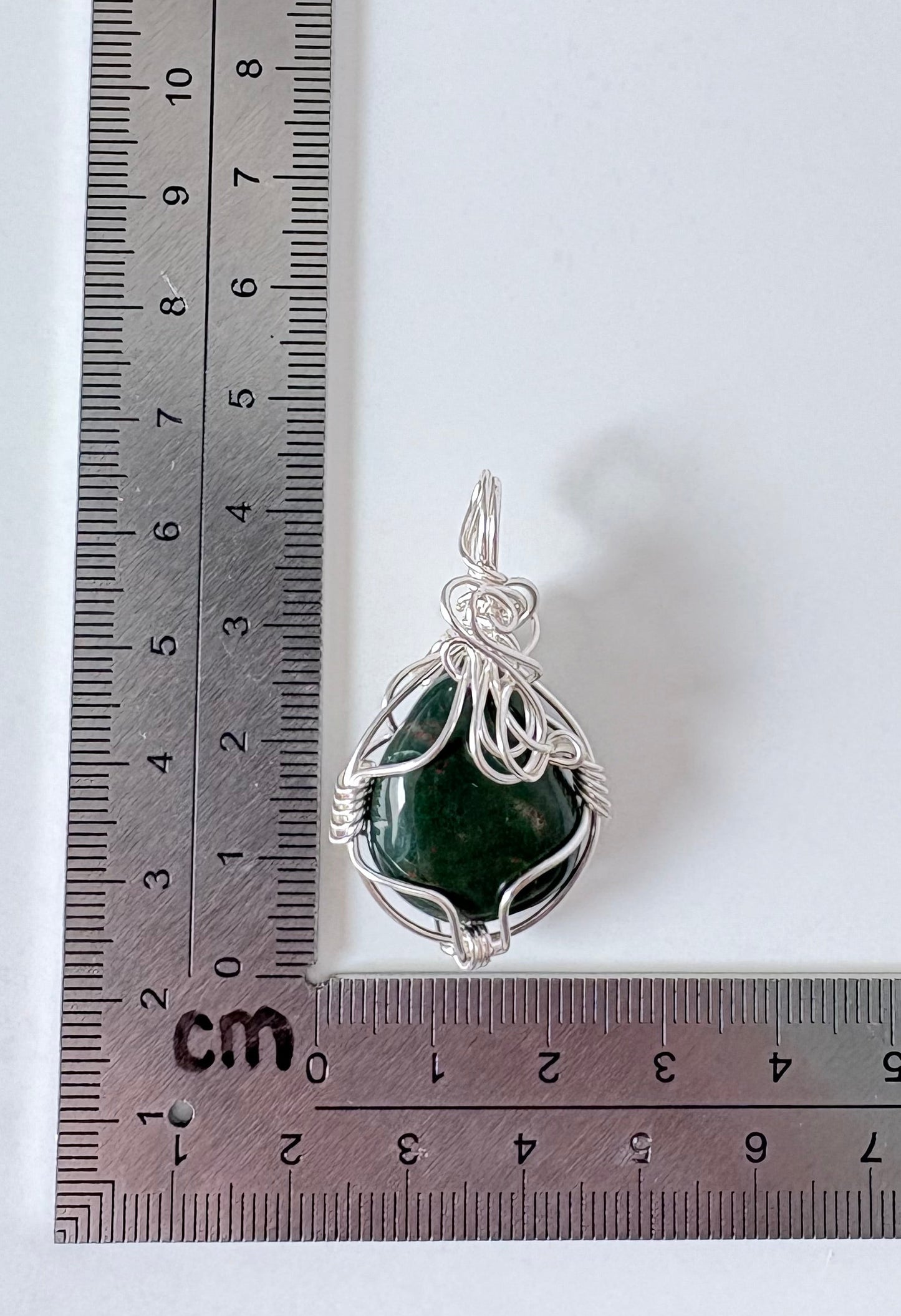 silver wire wrapped bloodstone pendant next to an "L" shaped ruler for scale all against a white background.