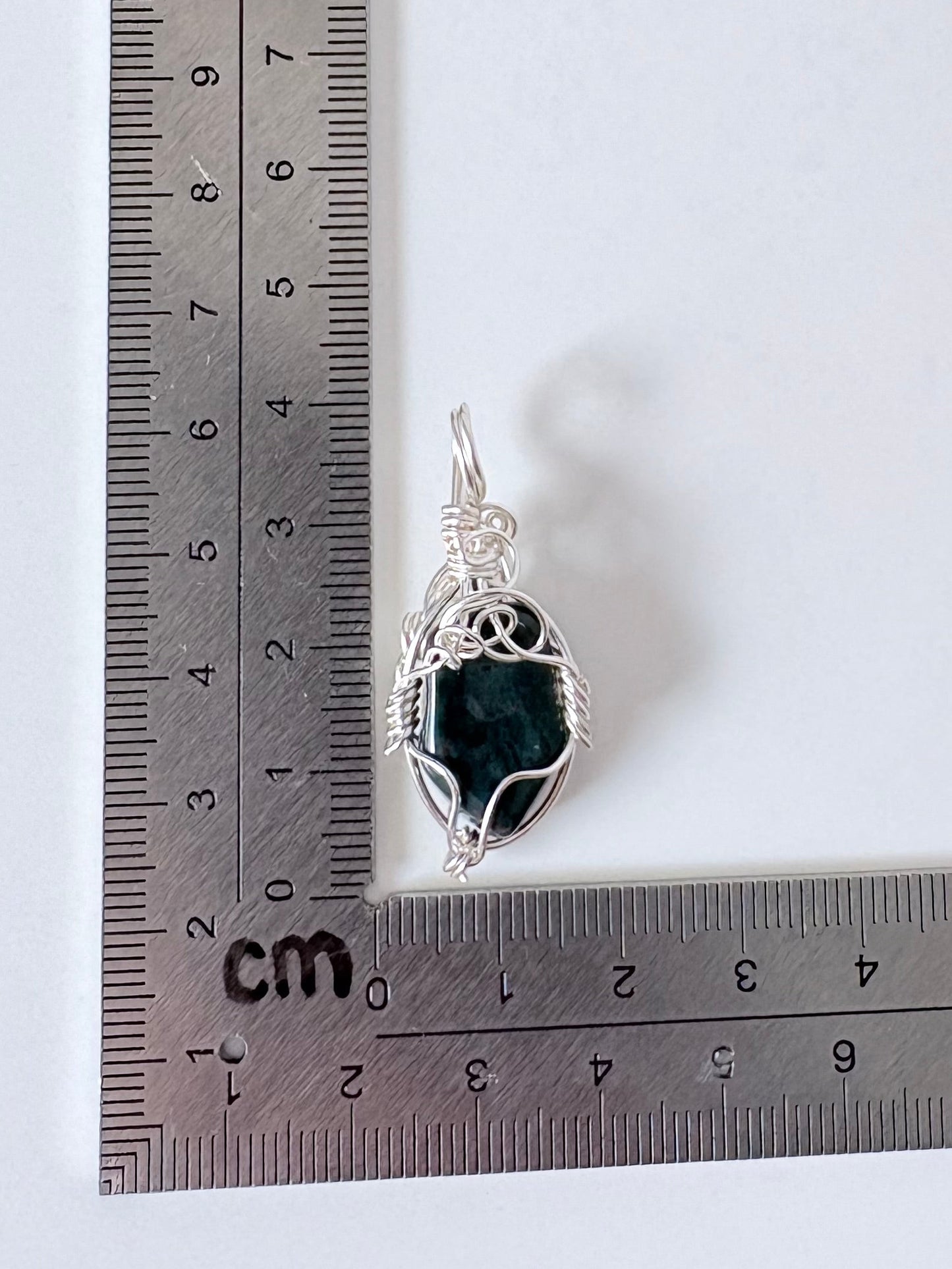 silver wire wrapped bloodstone pendant next to an "L" shaped ruler for scale all against a white background.