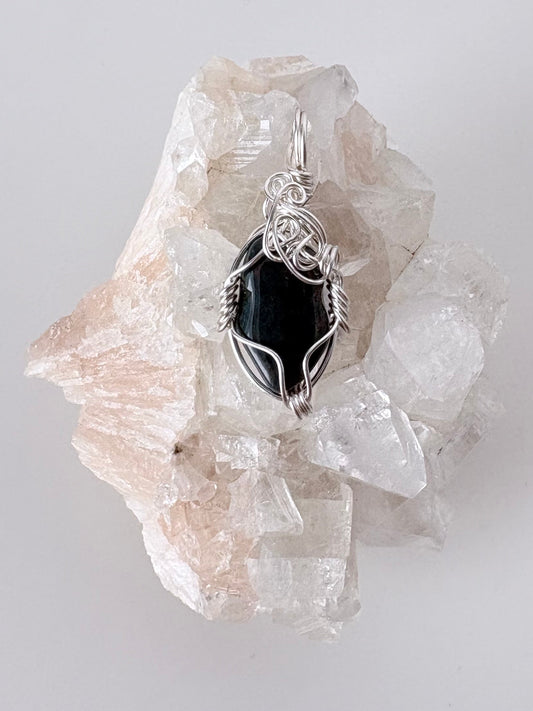 silver wire wrapped bloodstone pendant displayed on a clear apophyllite cluster all on a white surface.
