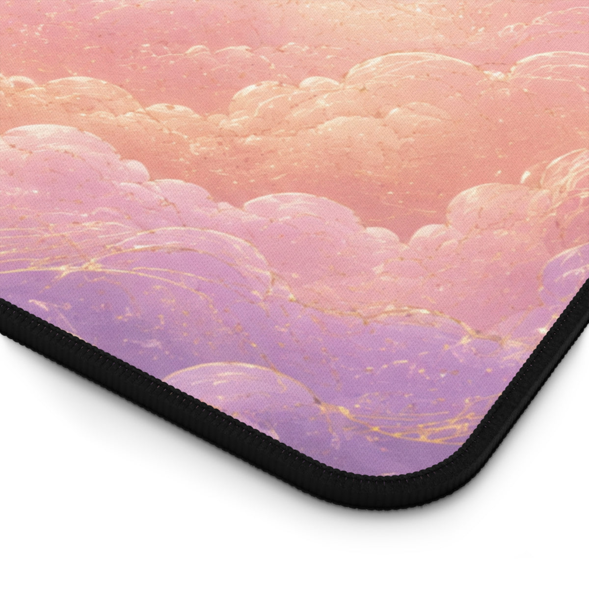 Close-up of the corner of a pastel celestial desk mat, showing soft pink and lavender clouds with delicate gold swirl and star details. The image highlights the textured fabric surface, rounded corner and black stitched edge of the 12 by 22 inch keyboard and mouse pad.