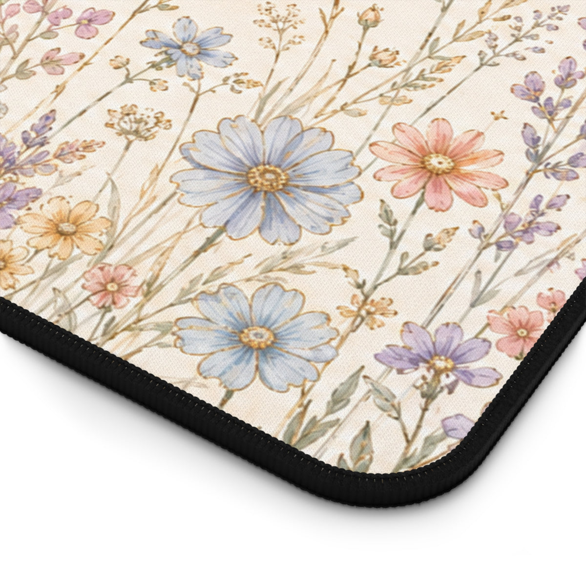 Close-up of the corner of a botanical desk mat, showing a soft cream background with pastel blue, pink, yellow and lavender wildflowers. The image highlights the mat’s textured fabric surface, rounded corner and black stitched edge for a detailed view of the floral design and finish.