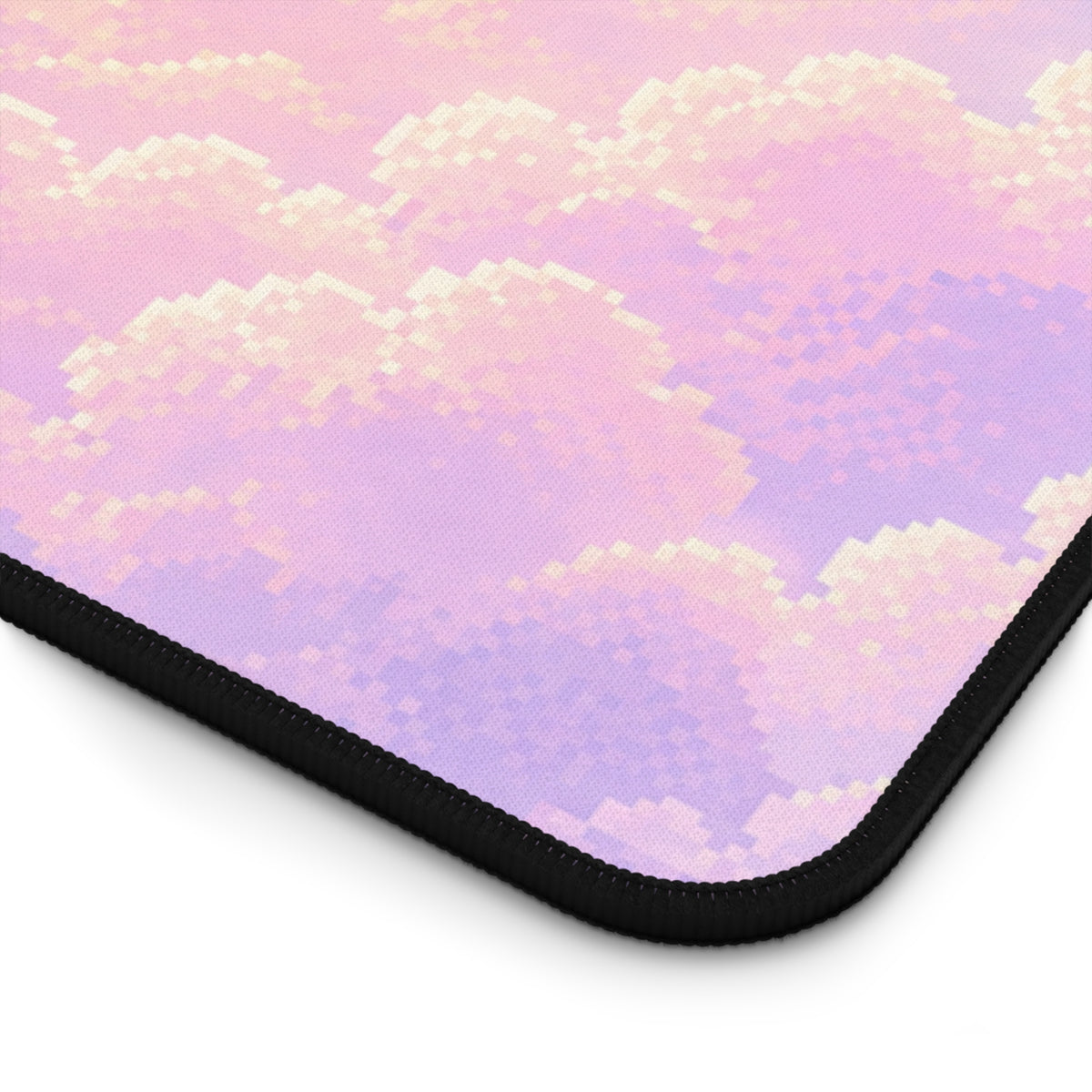 Close-up of the corner of a pastel celestial desk mat, showing the soft pixel-art cloud pattern in pink, lavender, cream and pale blue. The image highlights the mat’s textured fabric surface, rounded corner and thick black stitched border, giving a detailed view of the keyboard mat’s finish and edge construction.