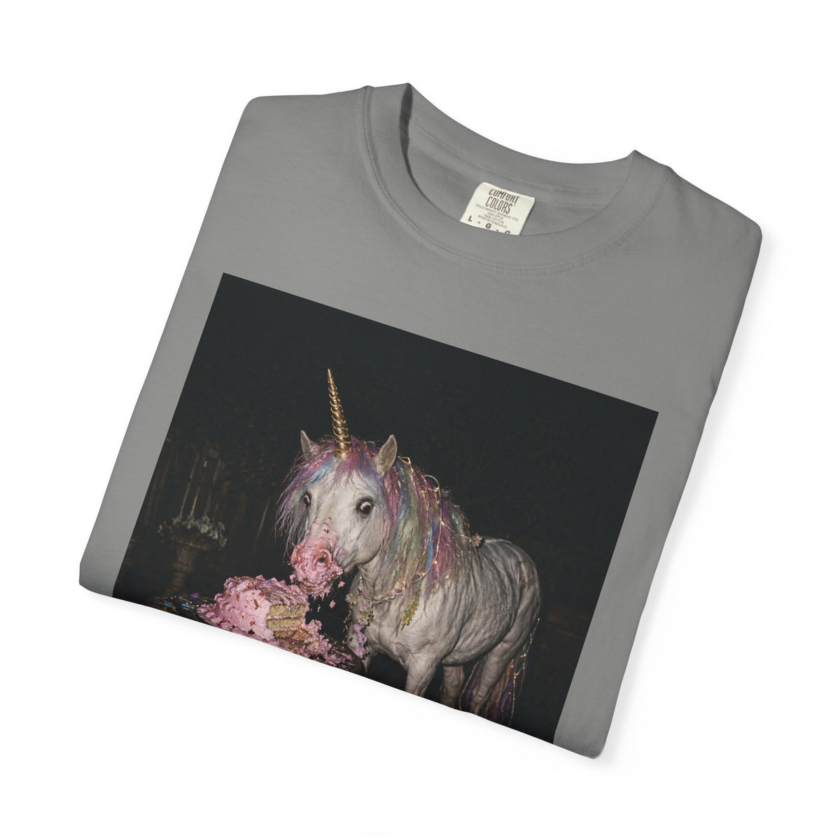 Front of folded grey graphic t-shirt with a retro-style photo of a unicorn stealing pink birthday cake at a dark party scene, shown on a white background.
