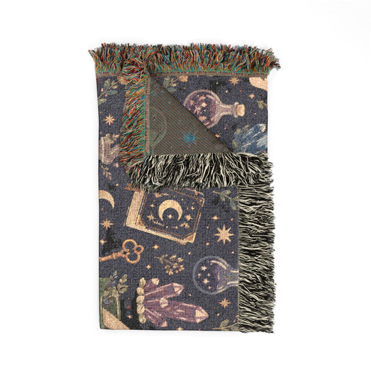 Folded Medium-Large sized witchy woven blanket with fringed edges, featuring an apothecary pattern with crystals, moons, potion bottles, spell books and stars. 50"x60"