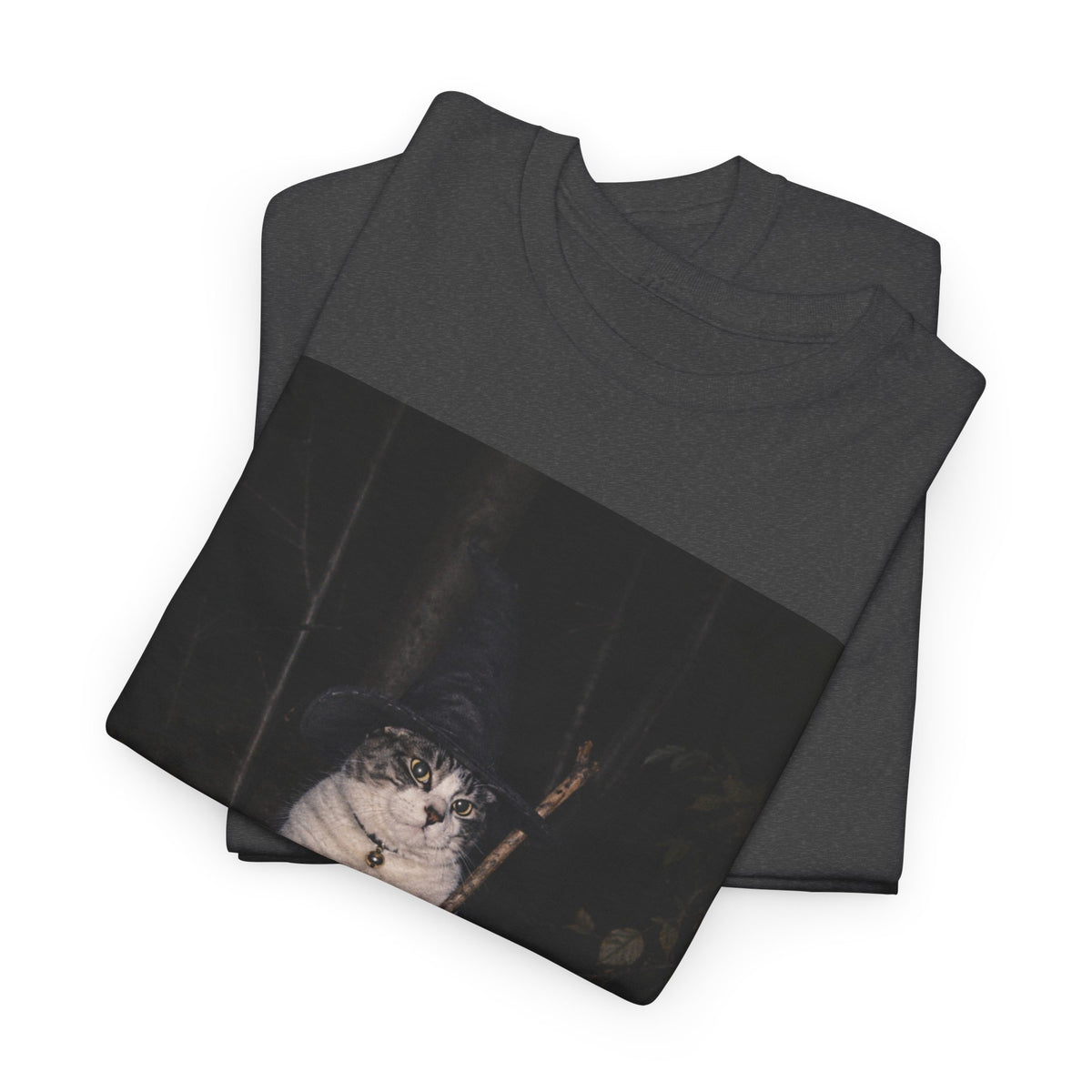 front of folded  graphic t-shirt featuring a photo of a cat wearing a black witch hat and a collar with a round bell, holding a broom in a dark woodland setting. The t-shirt is shown on a white background.
