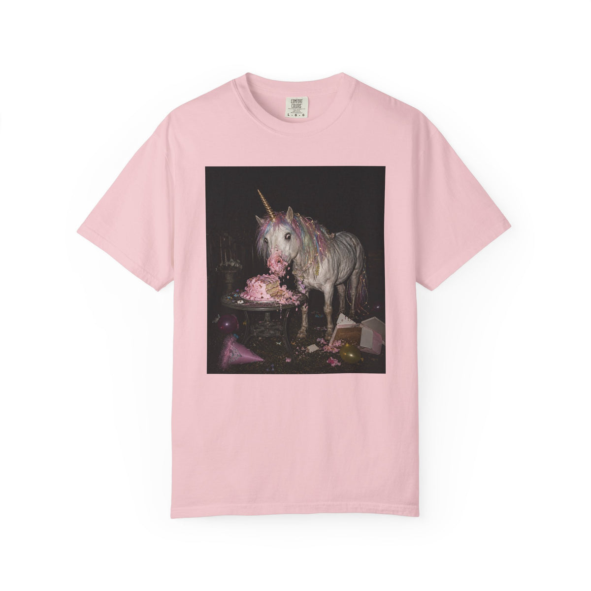 Pink graphic t-shirt with a retro-style photo of a unicorn stealing pink birthday cake at a dark party scene, shown on a white background.
