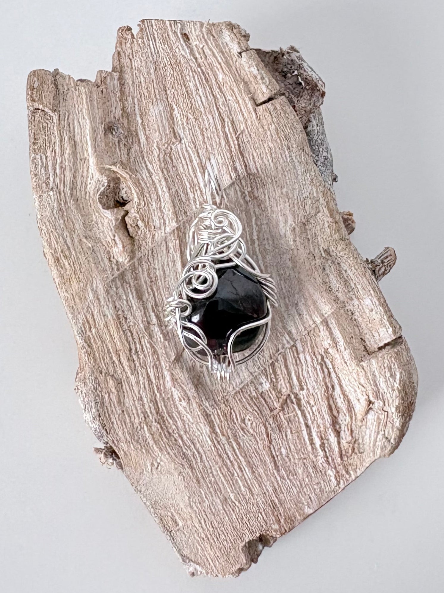 Silver wire-wrapped garnet pendant  on a piece of driftwood against a light background