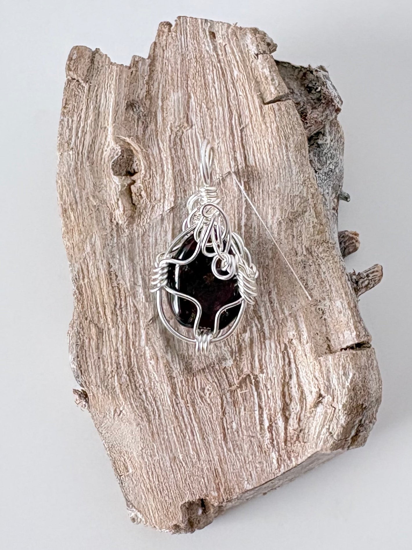 Silver wire-wrapped garnet pendant  on a piece of driftwood against a light background