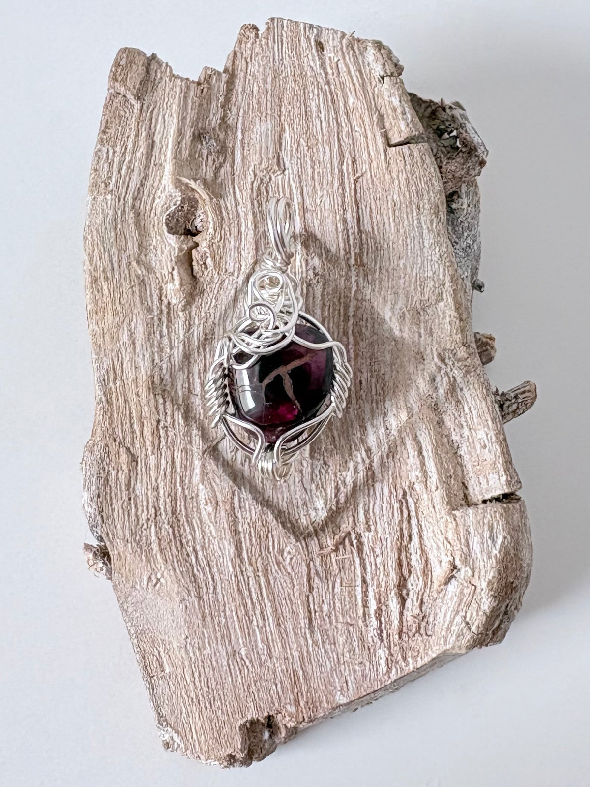 Silver wire-wrapped garnet pendant  on a piece of driftwood against a light background