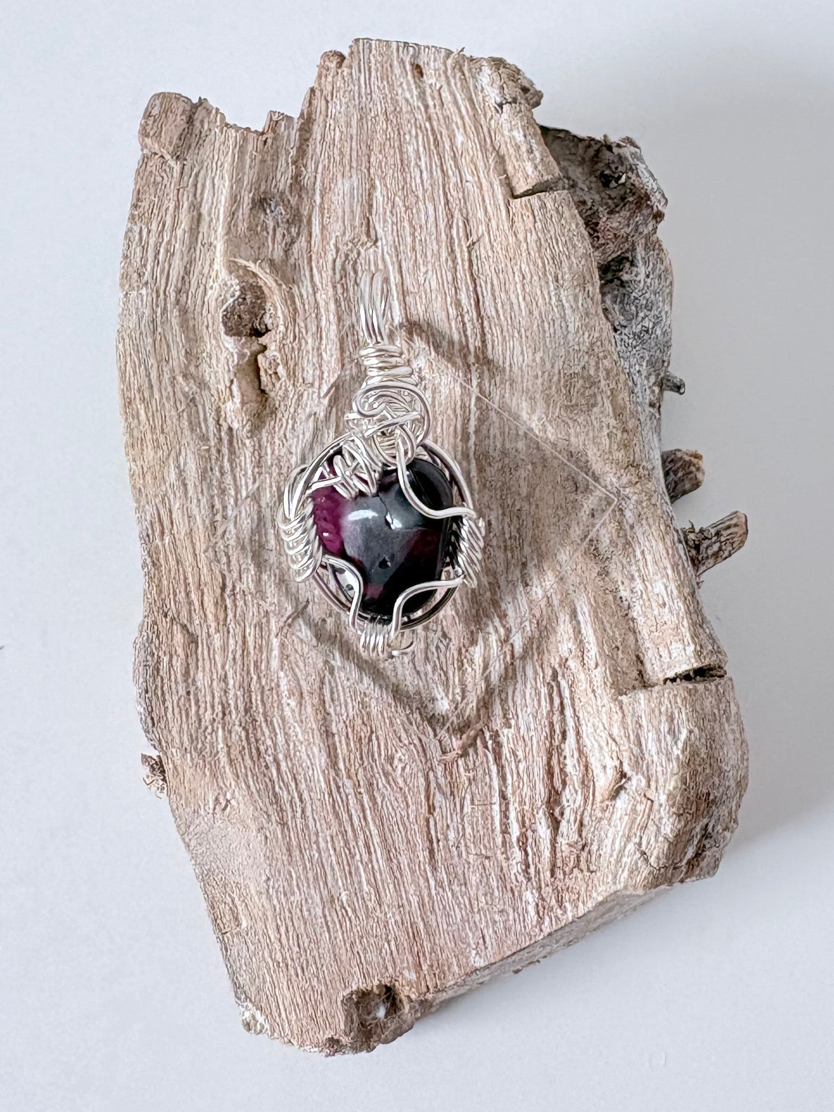 Silver wire-wrapped garnet pendant  on a piece of driftwood against a light background