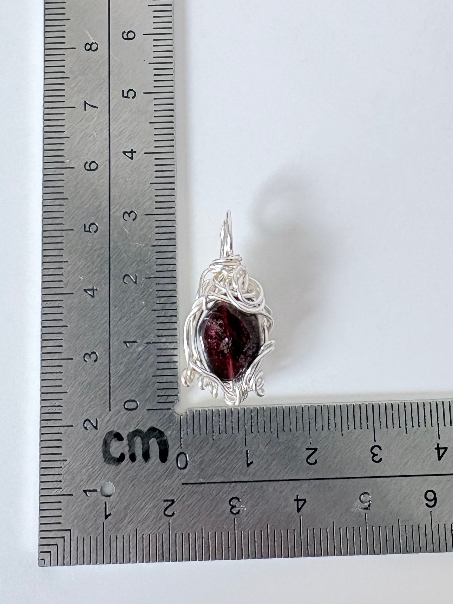 silver wire wrapped garnet pendant next to an "L" shaped ruler for scale all against a white background.