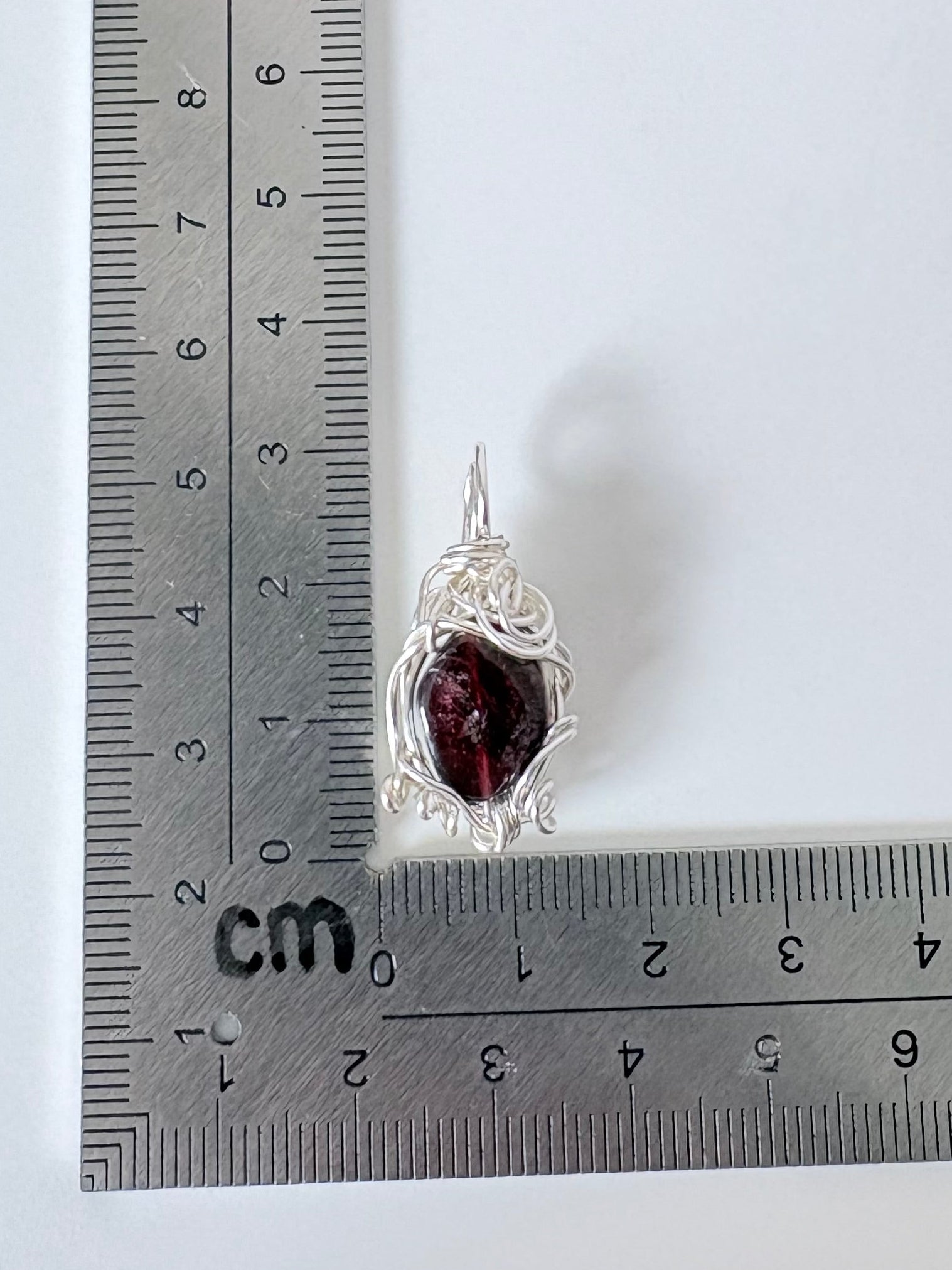silver wire wrapped garnet pendant next to an "L" shaped ruler for scale all against a white background.