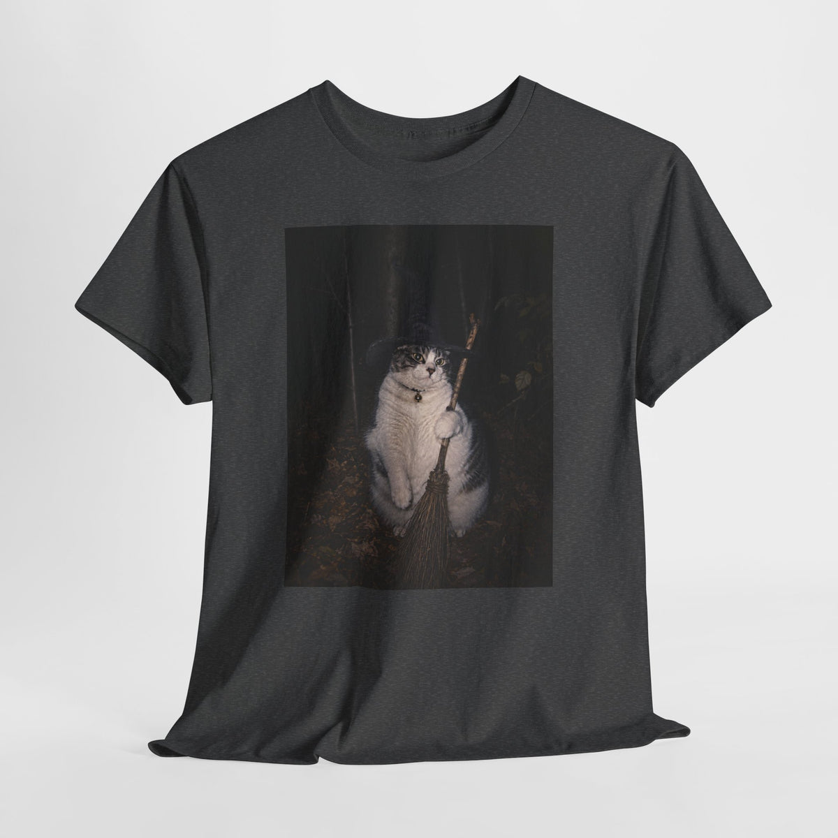 Front of a dark heather grey graphic t-shirt featuring a photo of a cat wearing a black witch hat and a collar with a round bell, holding a broom in a dark woodland setting. The t-shirt is shown on a white background.