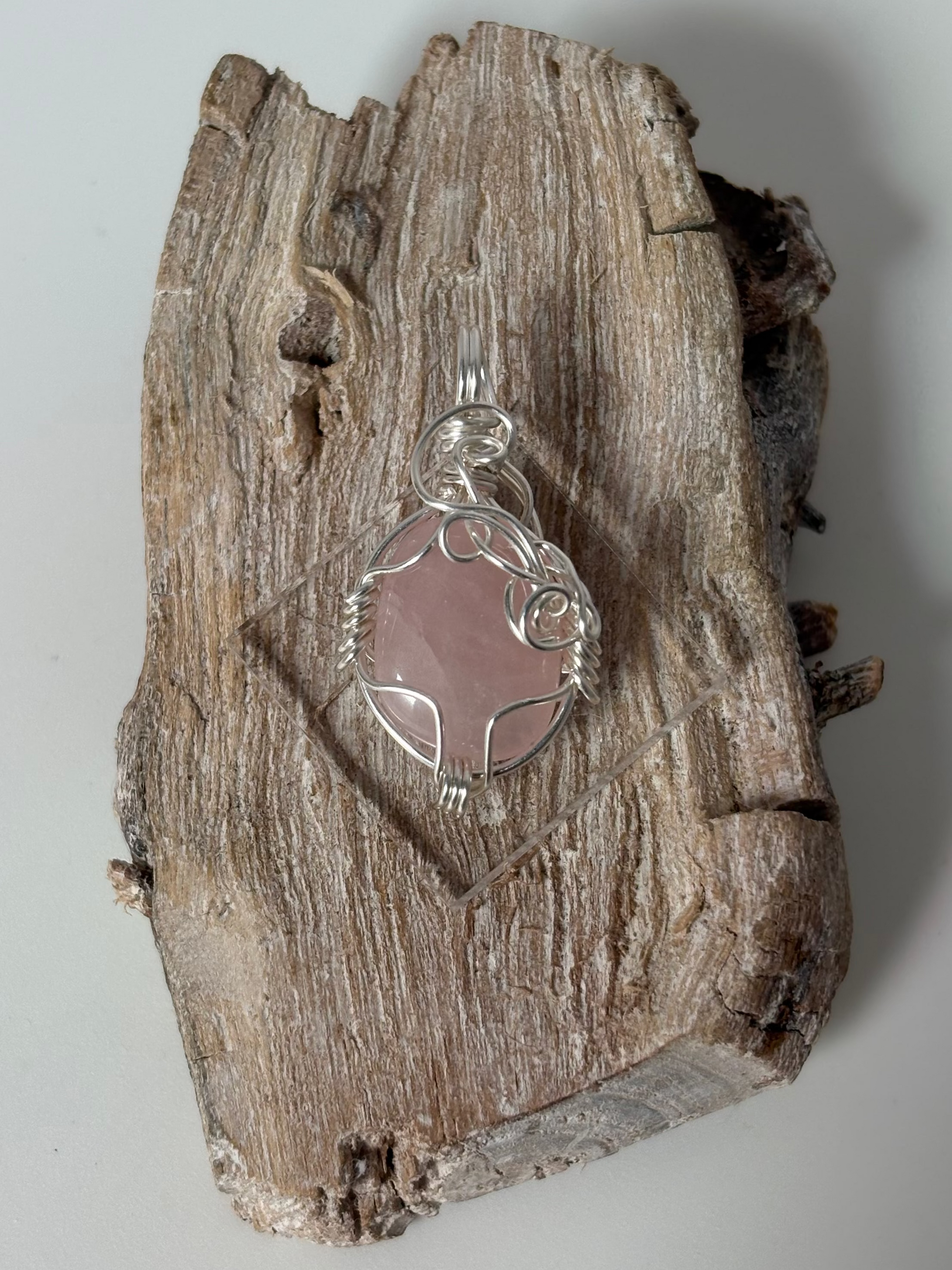 Silver pendant with a pink stone on a piece of driftwood against a white background