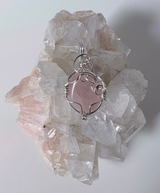 Crystal pendant with pink stone on a crystal cluster against a white background