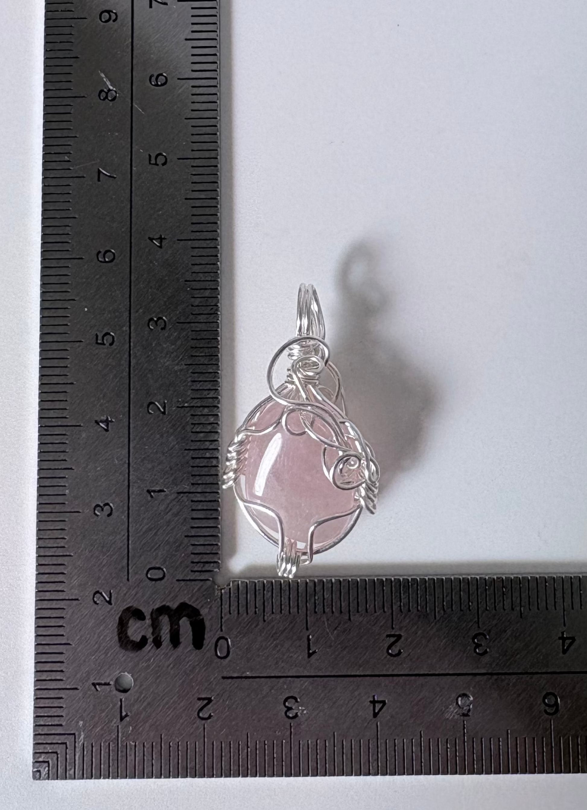 Silver pendant with pink stone on a ruler for scale on a white background