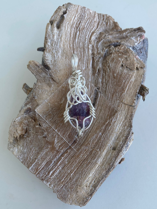 Lepidolite Pendant – Front view of a wire-wrapped purple stone pendant, handcrafted in silver-plated copper wire with a unique spiral design — photographed on a wood surface.