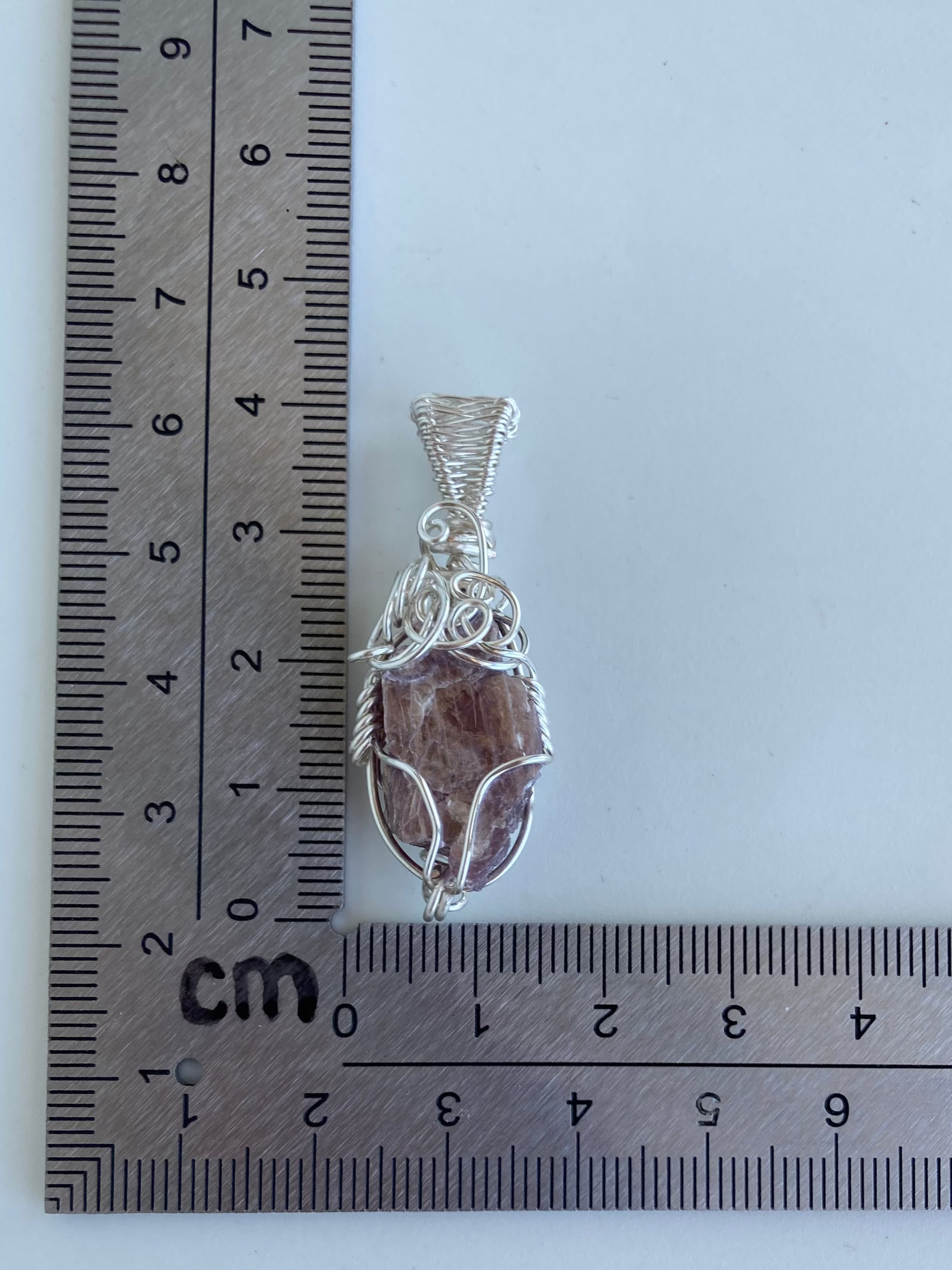 Lepidolite Pendant – Back view of a wire-wrapped purple lepidolite stone pendant shown beside an L-shaped centimeter ruler for size reference. Handcrafted in silver-plated copper wire with a unique spiral design — photographed on a white surface.