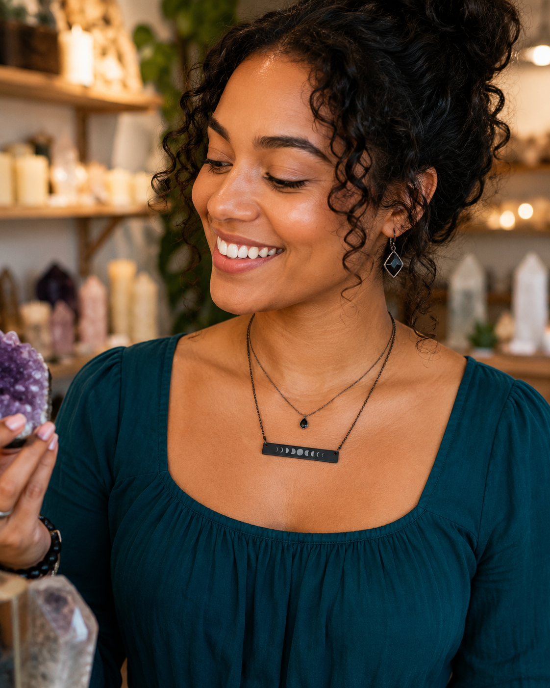 Woman wearing layered black necklaces in a store setting. One necklace is a horizontal bar moon phases pendant.