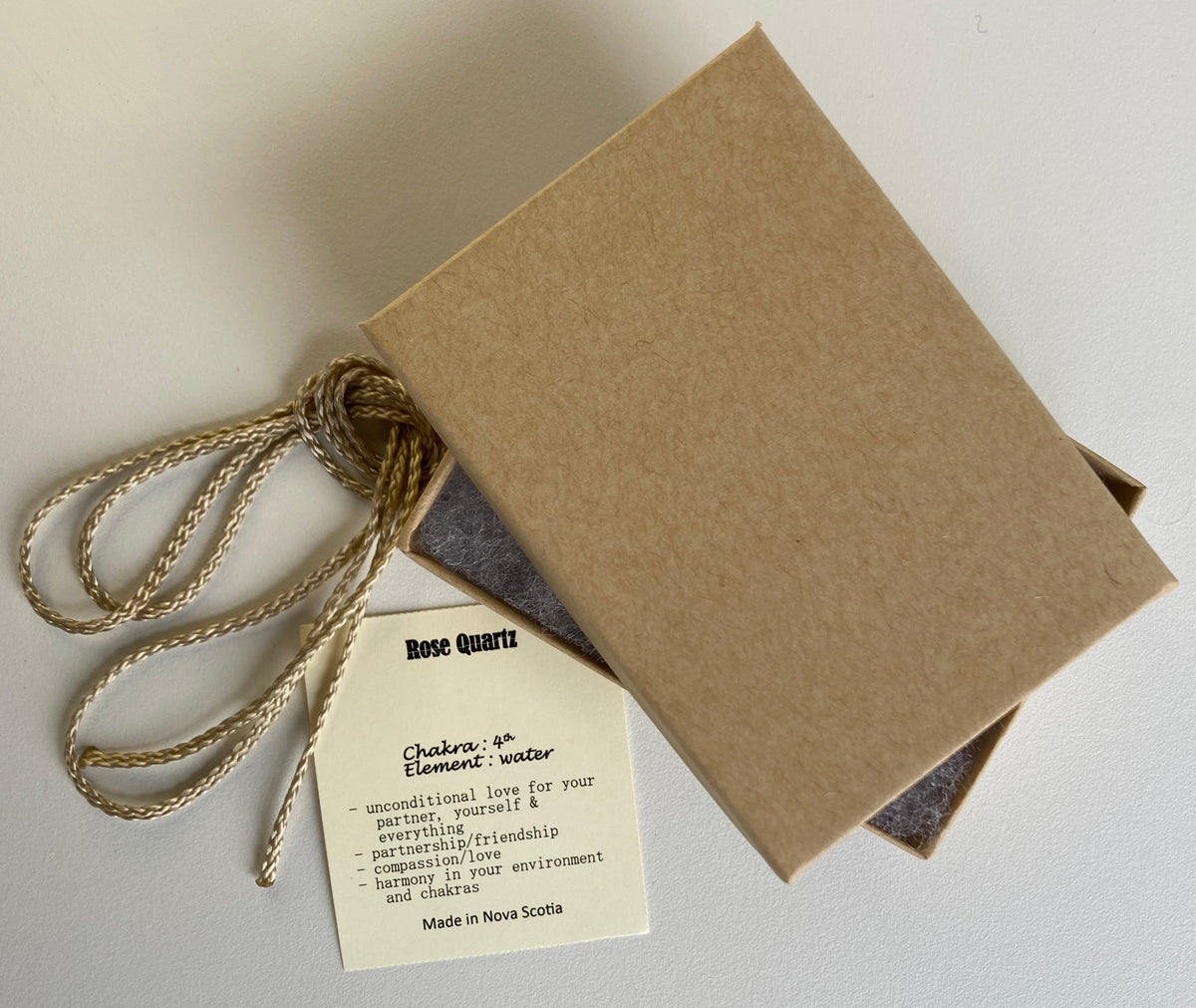 Kraft paper jewelry box with a rose quartz information tag and cream colour cord for a pendant on a white background
