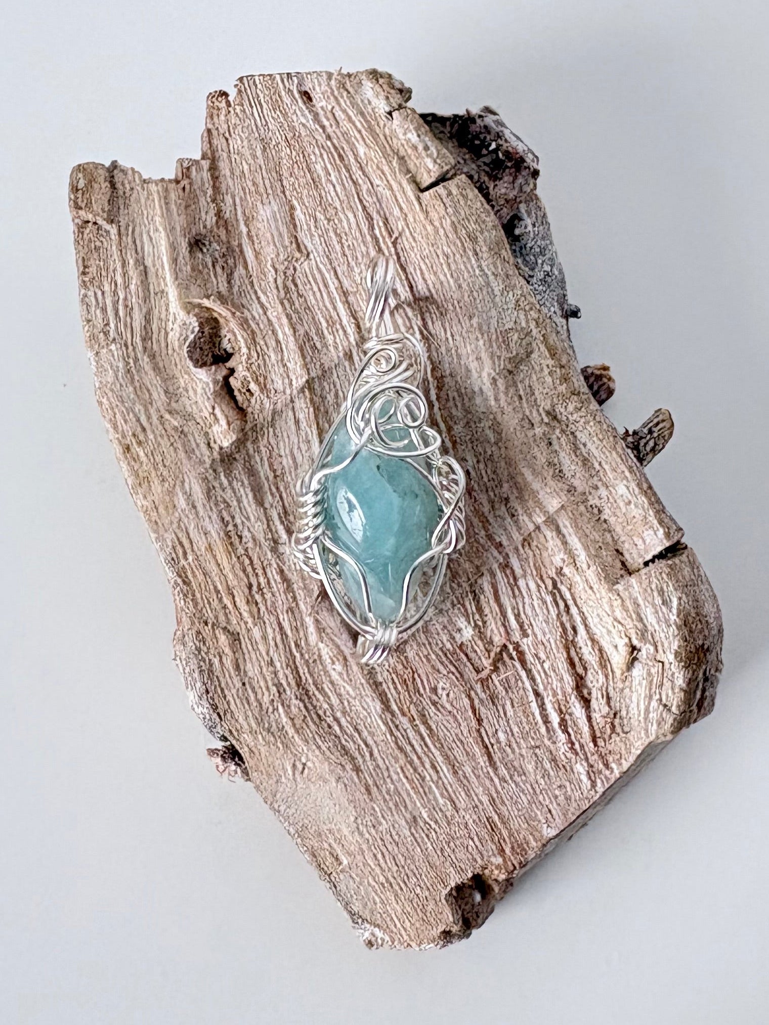 Silver wire-wrapped aquamarine pendant  on a piece of driftwood against a light background