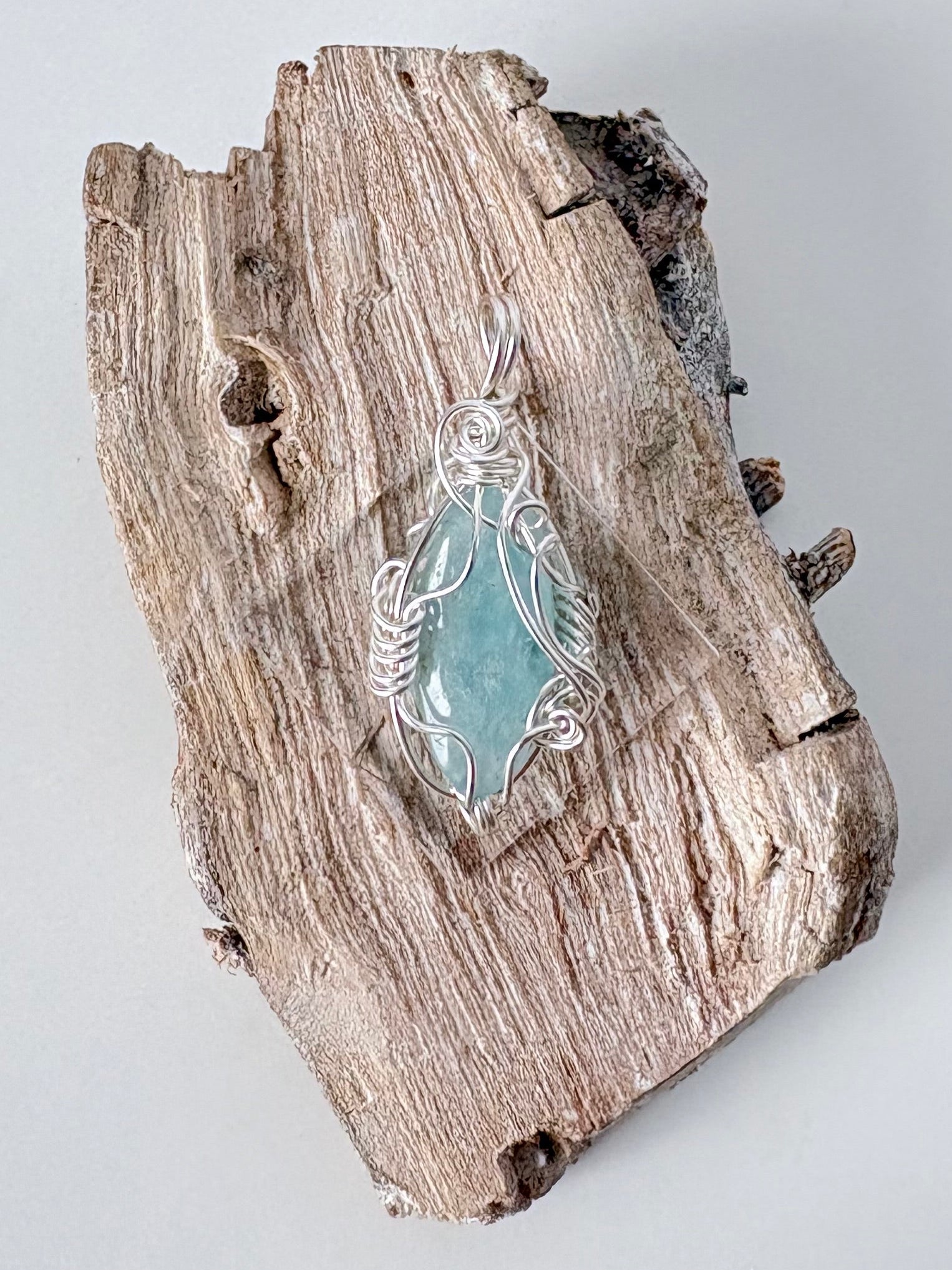 Silver wire-wrapped aquamarine pendant  on a piece of driftwood against a light background