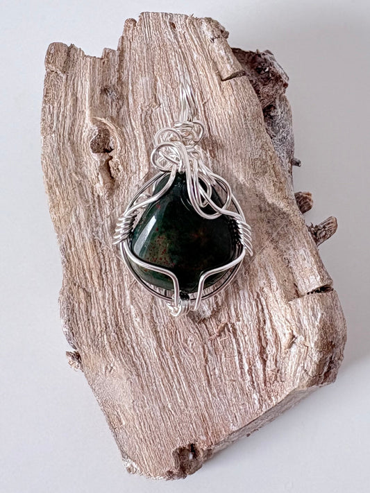 Silver wire-wrapped bloodstone pendant  on a piece of driftwood against a light background
