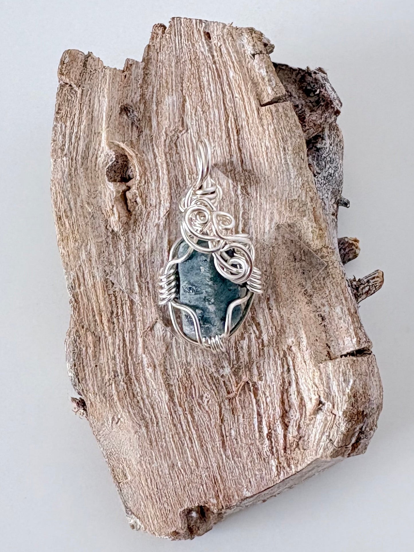 Silver wire-wrapped blue sapphire pendant  on a piece of driftwood against a light background