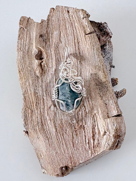 Silver wire-wrapped blue sapphire pendant  on a piece of driftwood against a light background