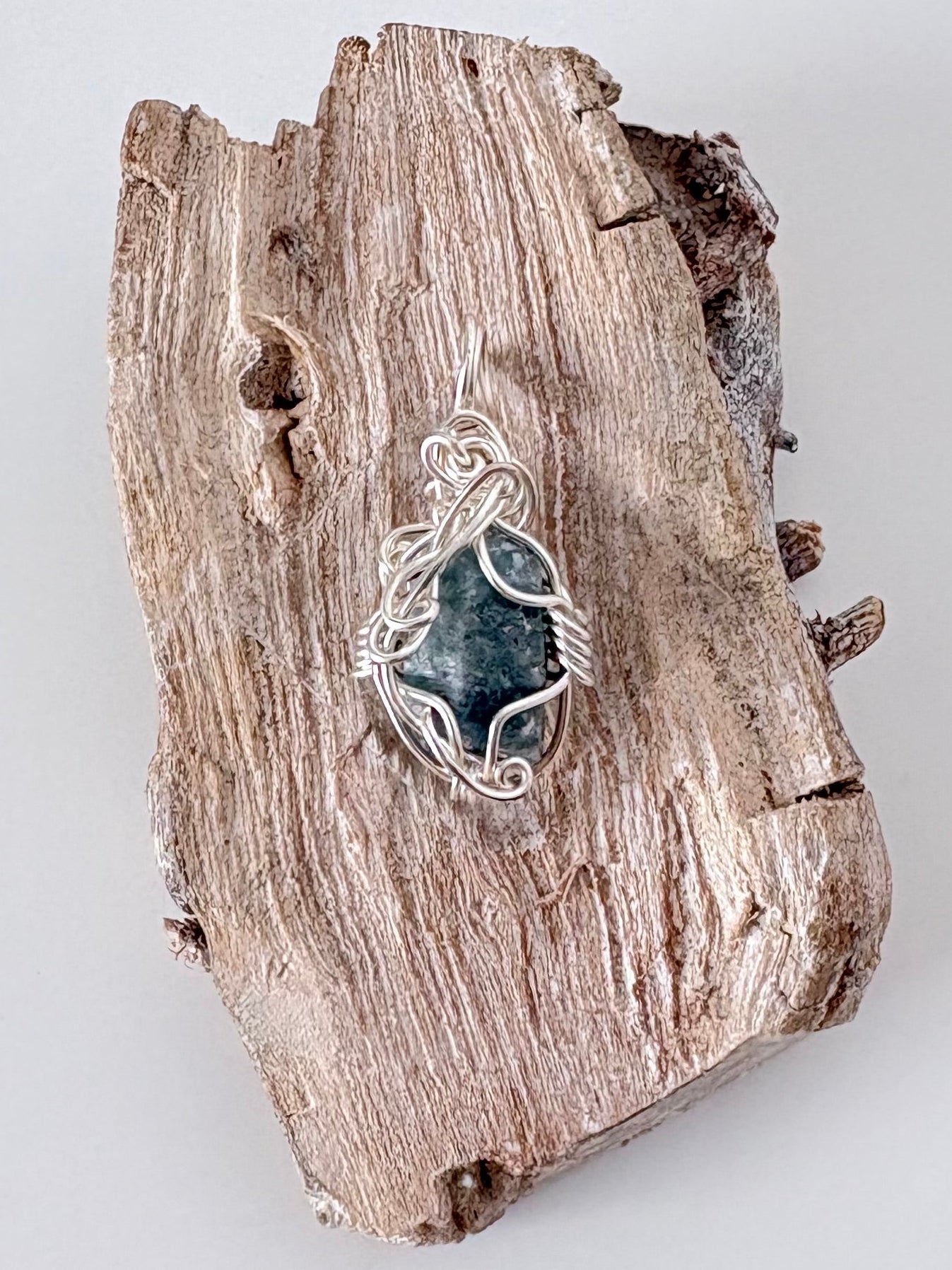 Silver wire-wrapped blue sapphire pendant  on a piece of driftwood against a light background