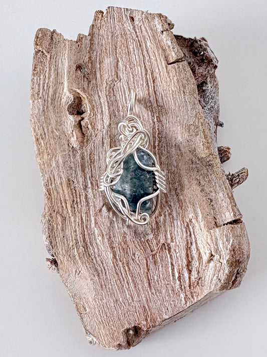 Silver wire-wrapped blue sapphire pendant  on a piece of driftwood against a light background