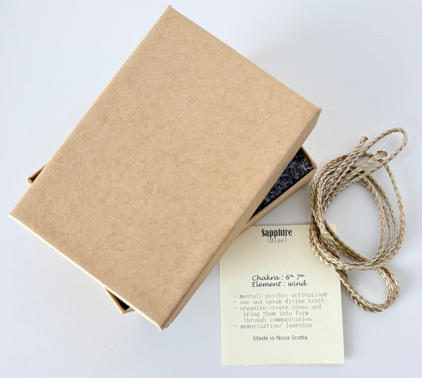 Kraft paper jewelry box with a blue sapphire information tag and cream colour cord for a pendant on a white background
