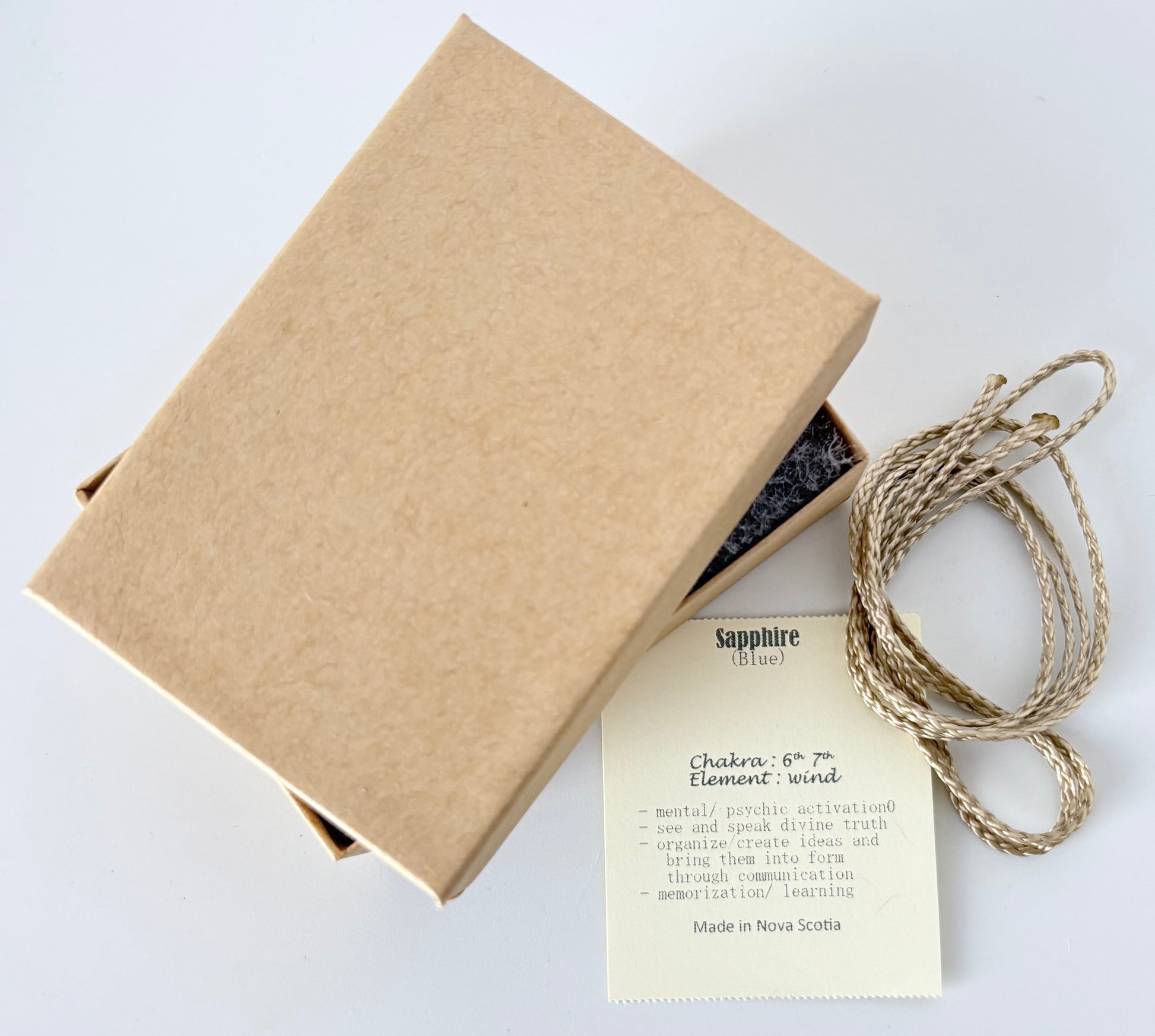 Kraft paper jewelry box with a blue sapphire information tag and cream colour cord for a pendant on a white background