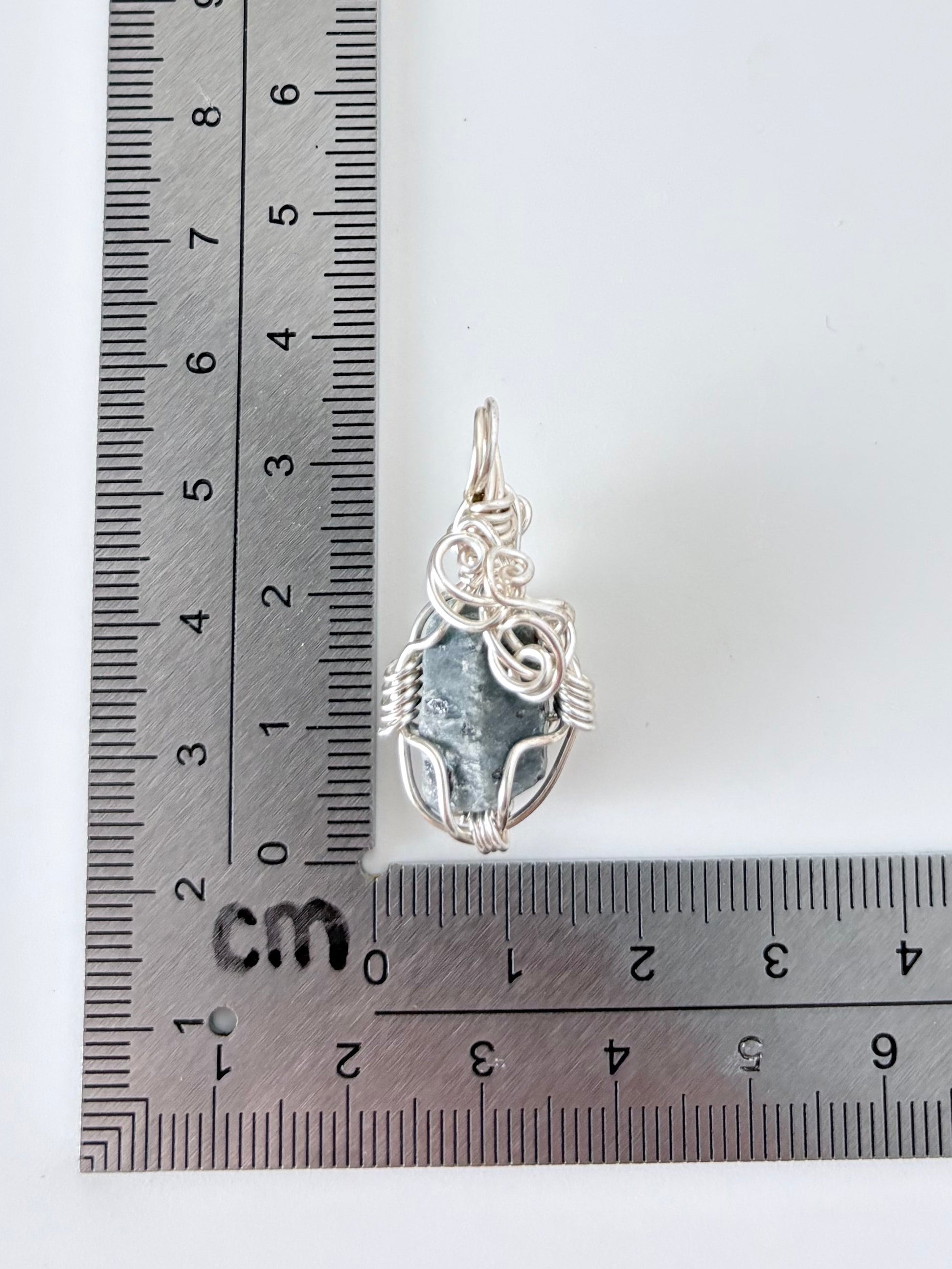 silver wire wrapped garnet pendant next to an "L" shaped ruler for scale all against a white background.