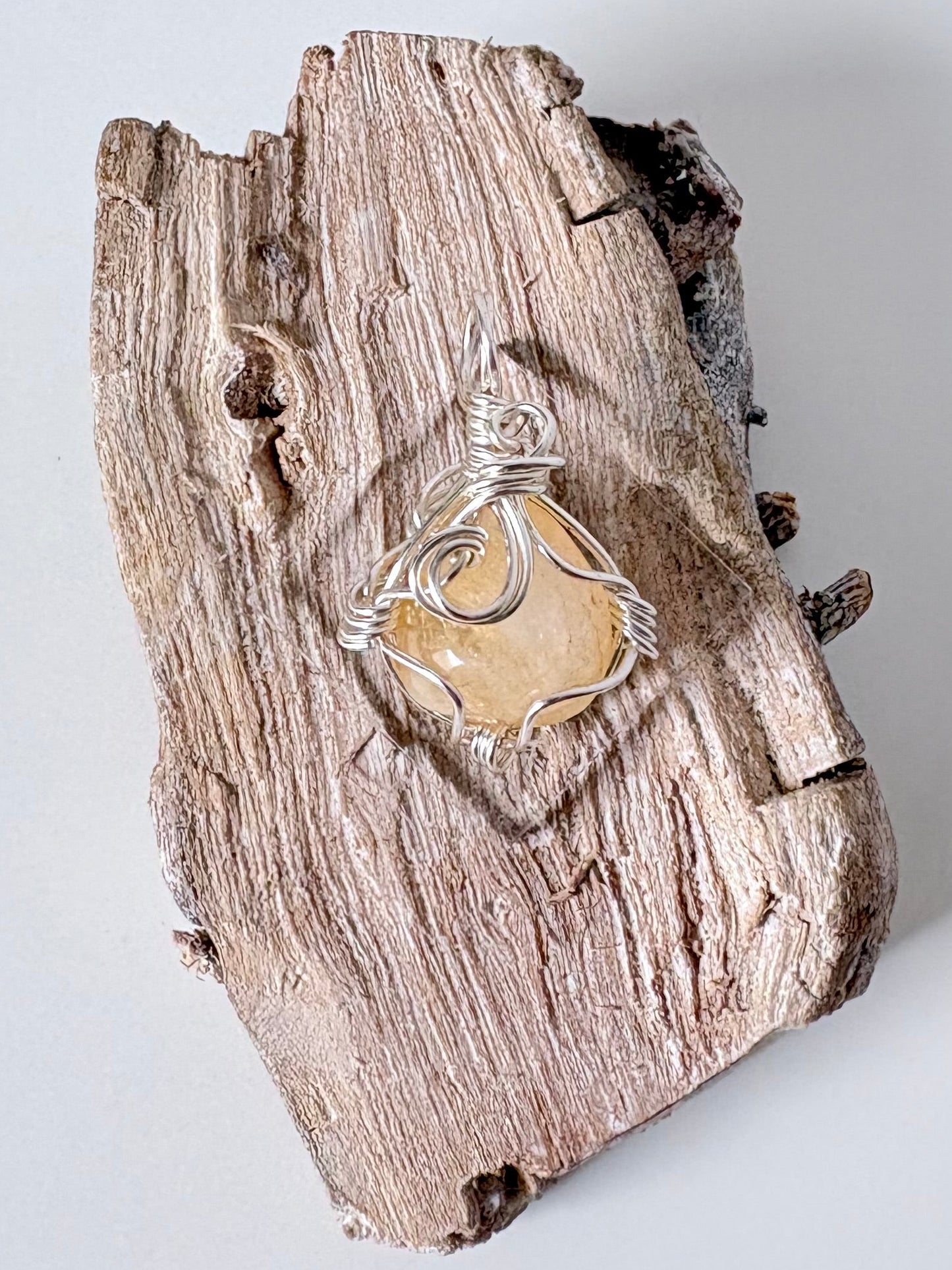 Silver wire-wrapped citrine pendant  on a piece of driftwood against a light background