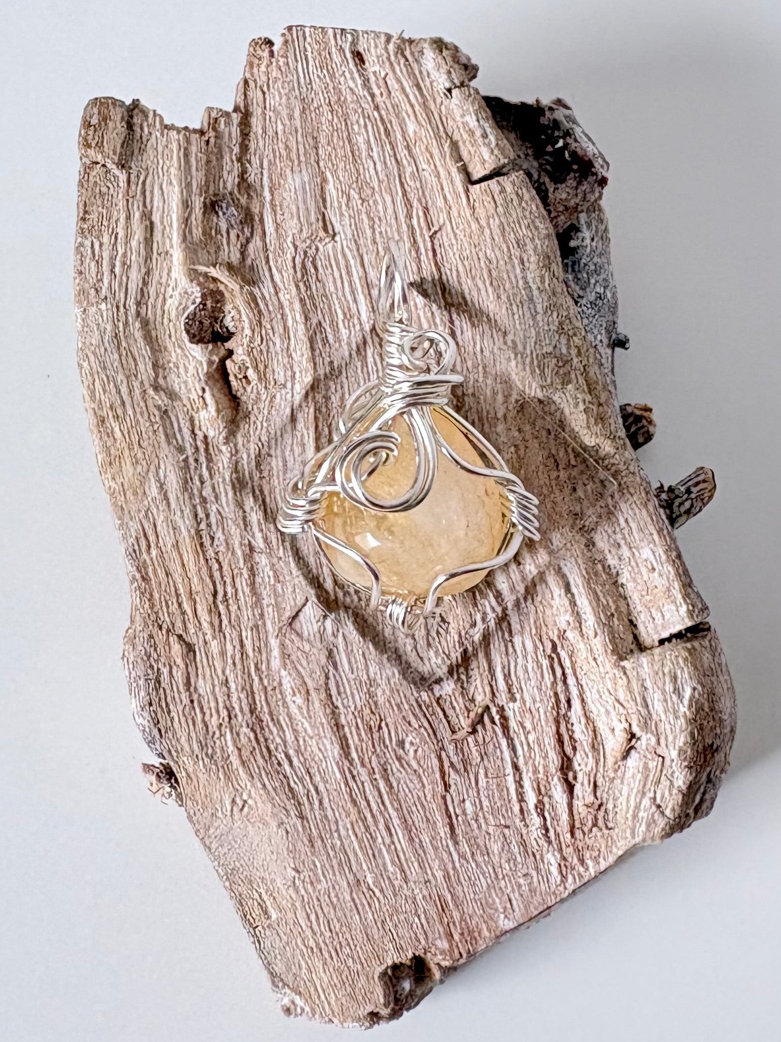 Silver wire-wrapped citrine pendant  on a piece of driftwood against a light background