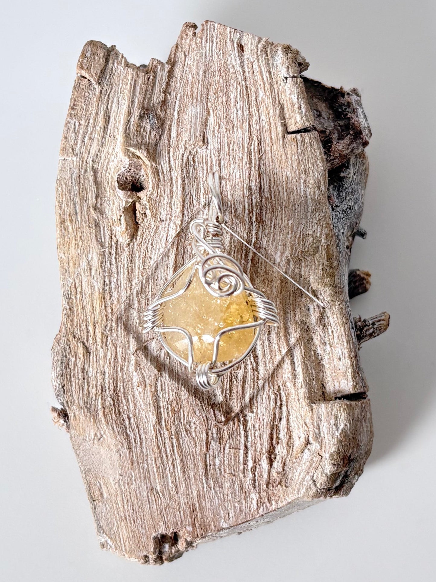Silver wire-wrapped citrine pendant  on a piece of driftwood against a light background