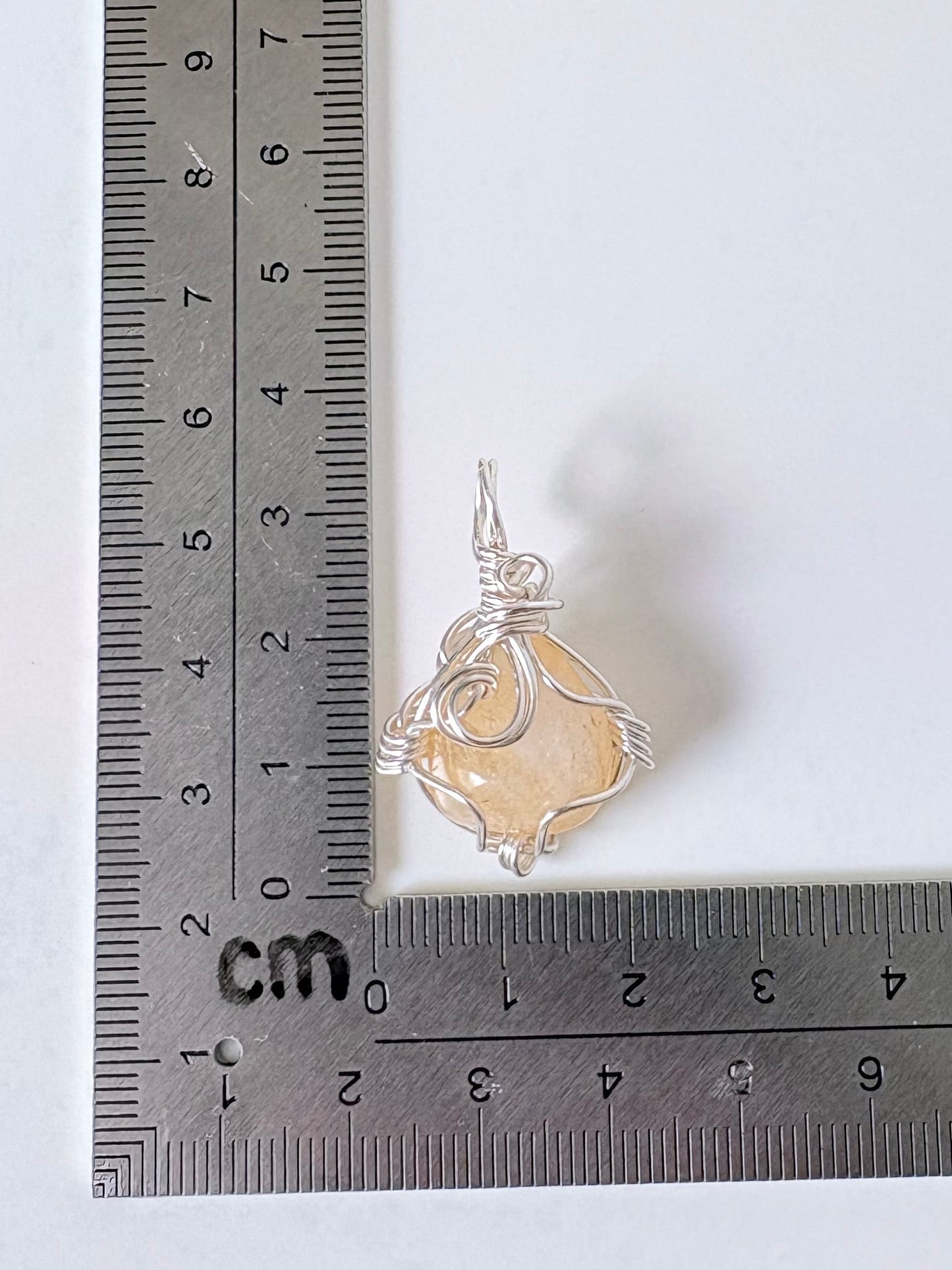 silver wire wrapped citrine pendant next to an "L" shaped ruler for scale all against a white background.